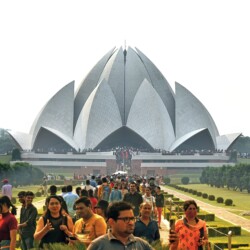 Thousands of daily visitors gather at the Lotus Temple, making it one of the world's most visited religious sites. Lotus Temple Delhi wide establishing shot with visitors and crowds for scale