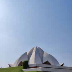 Side perspective of the Lotus Temple revealing the complex geometry of its 27 interconnected marble petals. Lotus Temple Delhi exterior side view showing curved marble petals against blue sky
